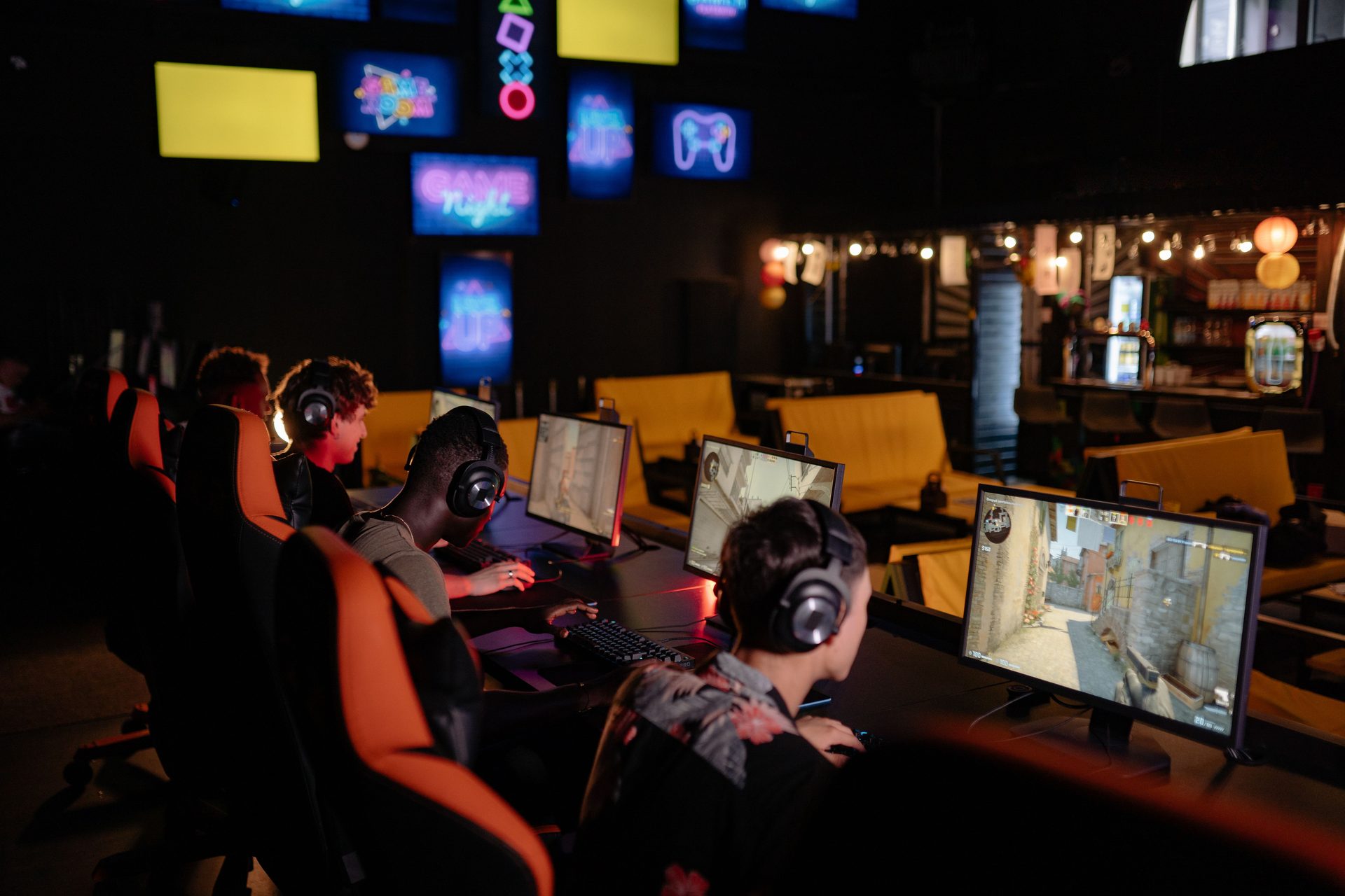 Rows of neon-lit gaming PCs in a dark underground hall, players in headsets at glowing stations